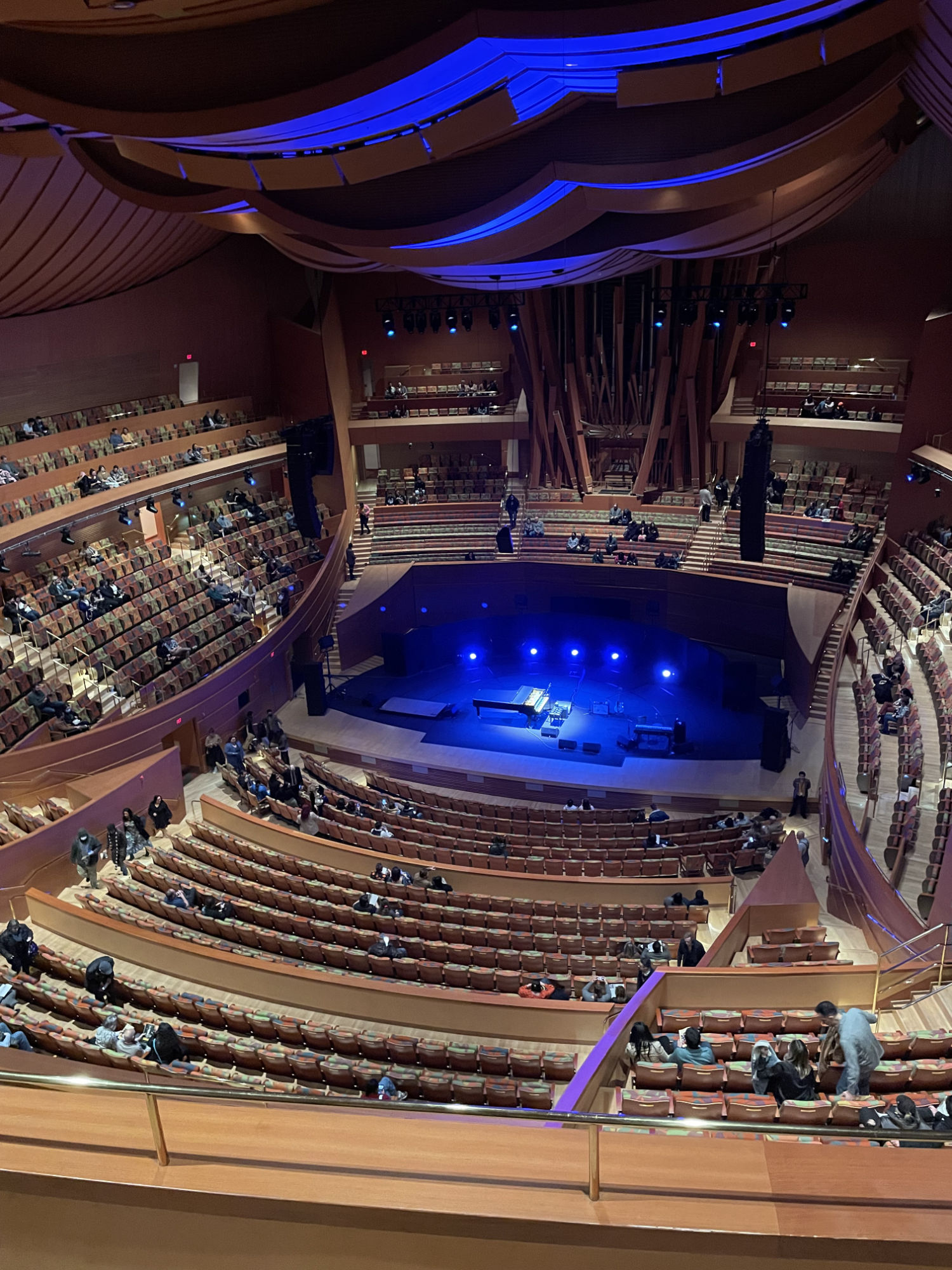 The Walt Disney Concert Hall from a balcony seat. The seats are in aligned in curves. On the sage, there is a pinao and an electronic keyboard.
